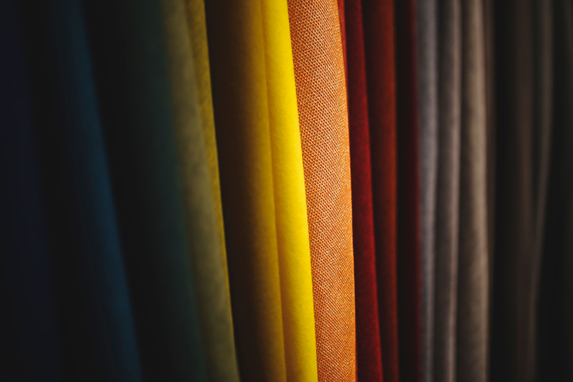 Bolts of coloured fabric standing side by side in deep light